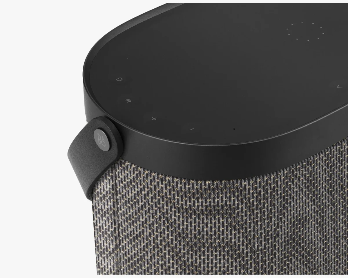 Black Bang & Olufsen portable speaker featuring a textured fabric exterior, a top touch control panel, and a branded leather carry handle.