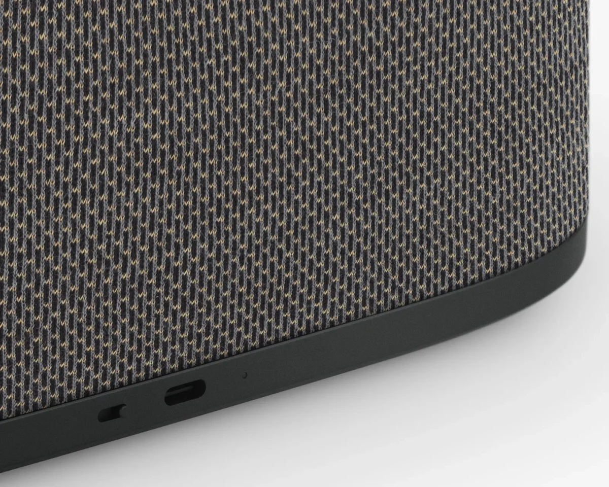 Close-up of a speaker featuring a grey and tan woven fabric exterior and a black plastic base with two input ports.