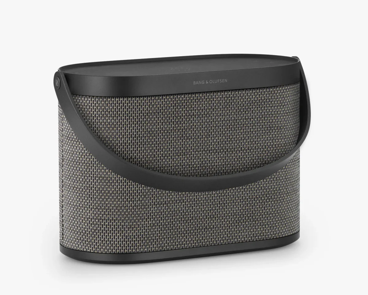 Bang & Olufsen portable speaker featuring a textured grey mesh body, a black top, and a curved carrying handle.