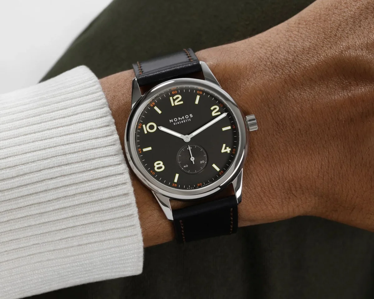 Nomos Glashütte watch with a black dial, silver hands, and a black leather strap on a wrist.