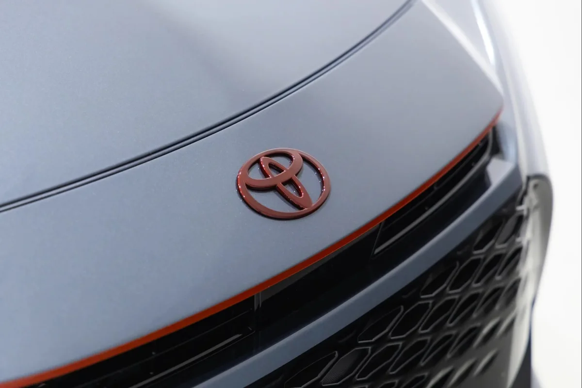 Close-up of a grey car hood featuring a dark red Toyota emblem above a thin orange trim line and a black honeycomb grille.