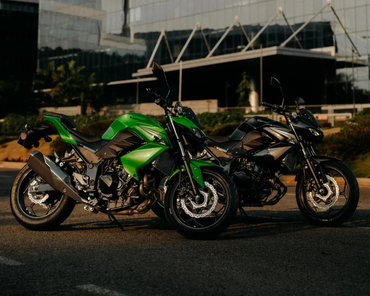 Two Kawasaki motorcycles, one lime green and one black, parked side by side on a paved lot.