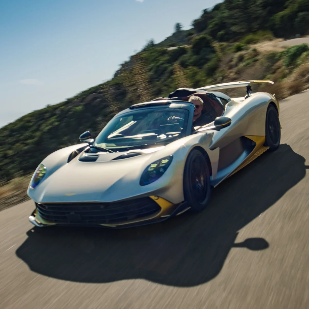 Silver and gold sports car driving fast on a winding mountain road.