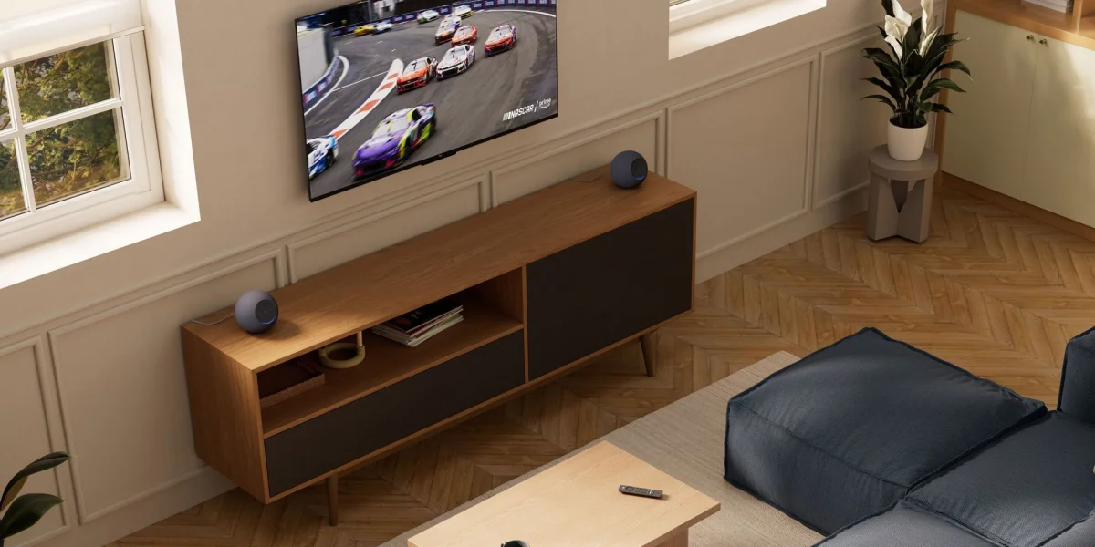 Modern living room with wall-mounted TV, wood media console, blue sofa, and potted plant.