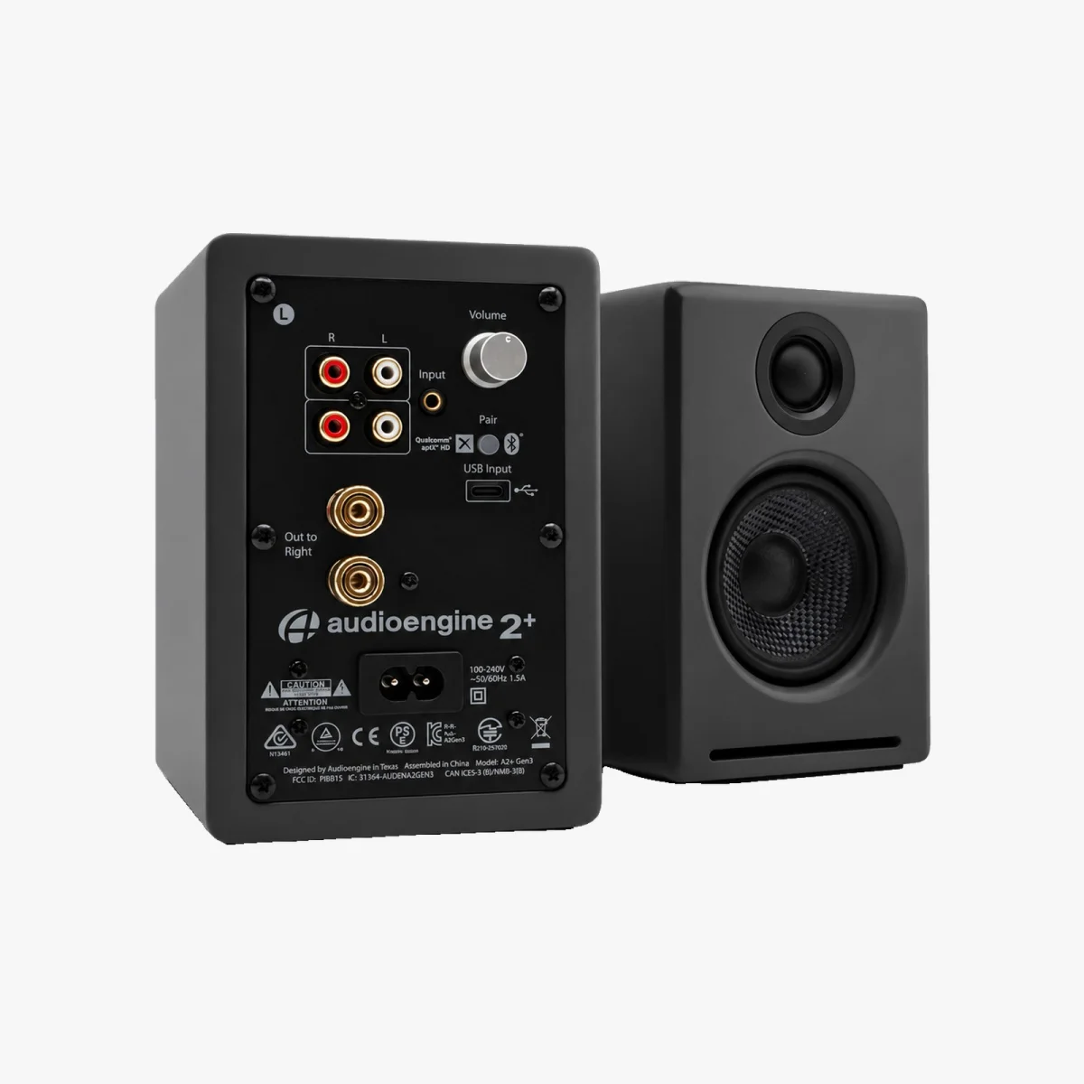 Pair of black Audioengine 2+ speakers; one faces forward showing the front grille, while the other is turned to reveal rear input/output ports, volume knob, and pairing button.