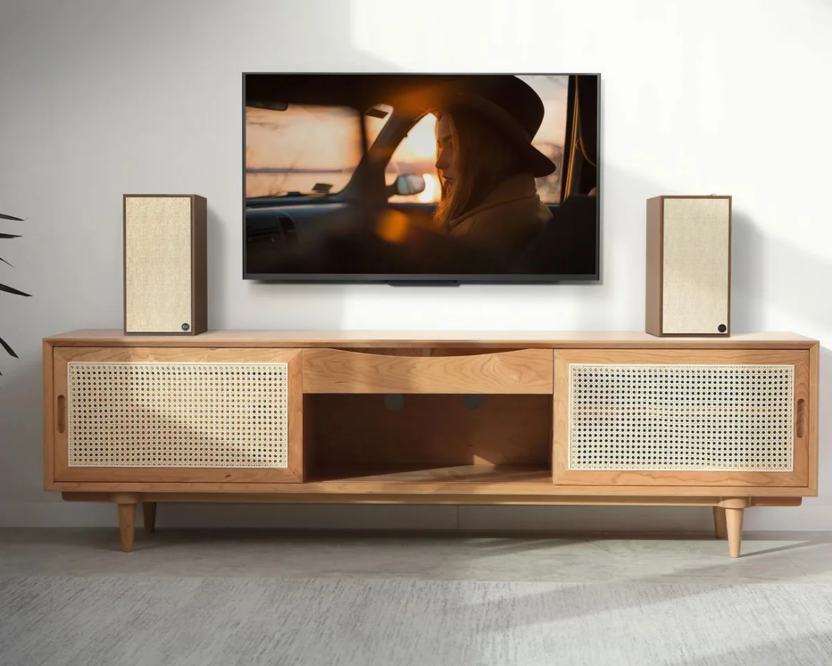 Light wood TV stand with woven cane sliding doors and two beige speakers on top, beneath a wall-mounted flat screen TV.