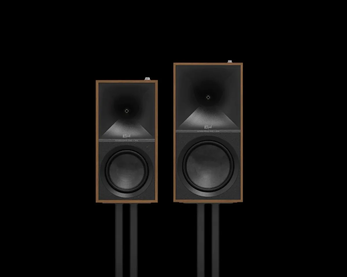 Pair of Klipsch speakers with wooden frames and black front panels, mounted on black stands against a black background.