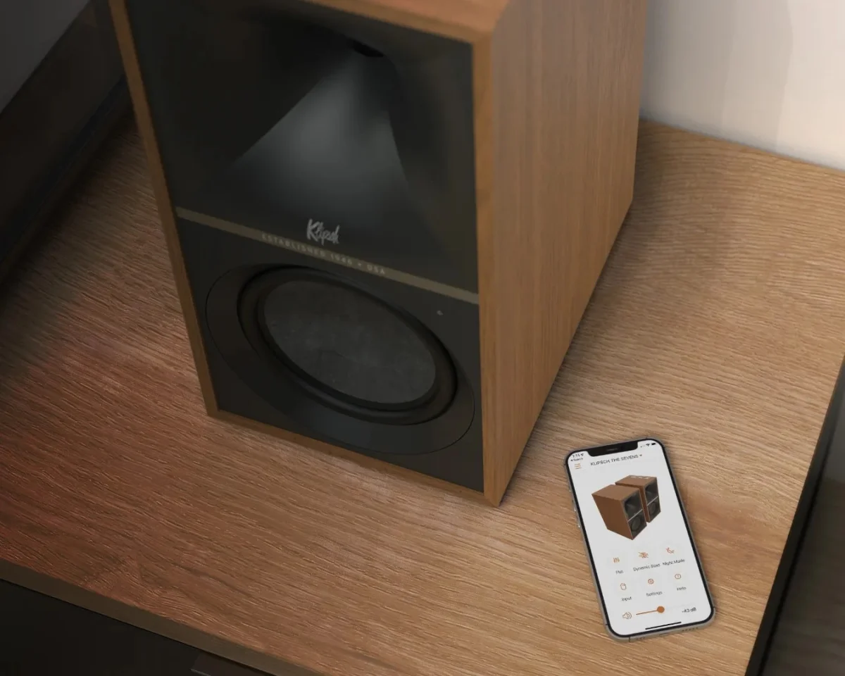 Wood-finished Klipsch speaker on a wooden surface next to a smartphone displaying speaker control app.