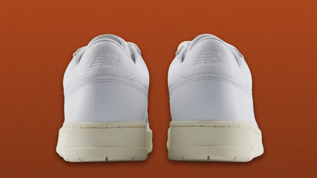 White sneakers with a smooth finish, shown from the back on a solid burnt orange background.