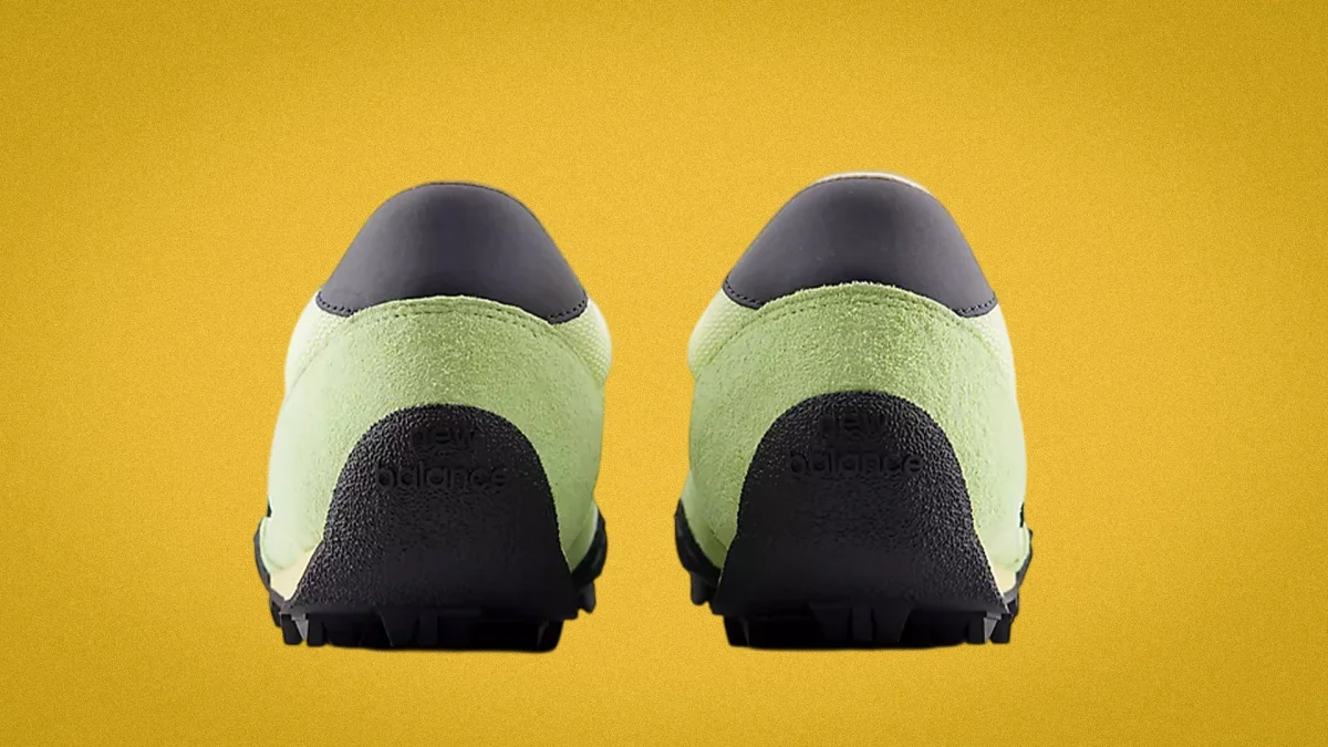 Pair of light green and black New Balance sneakers shown from the back on a yellow background.