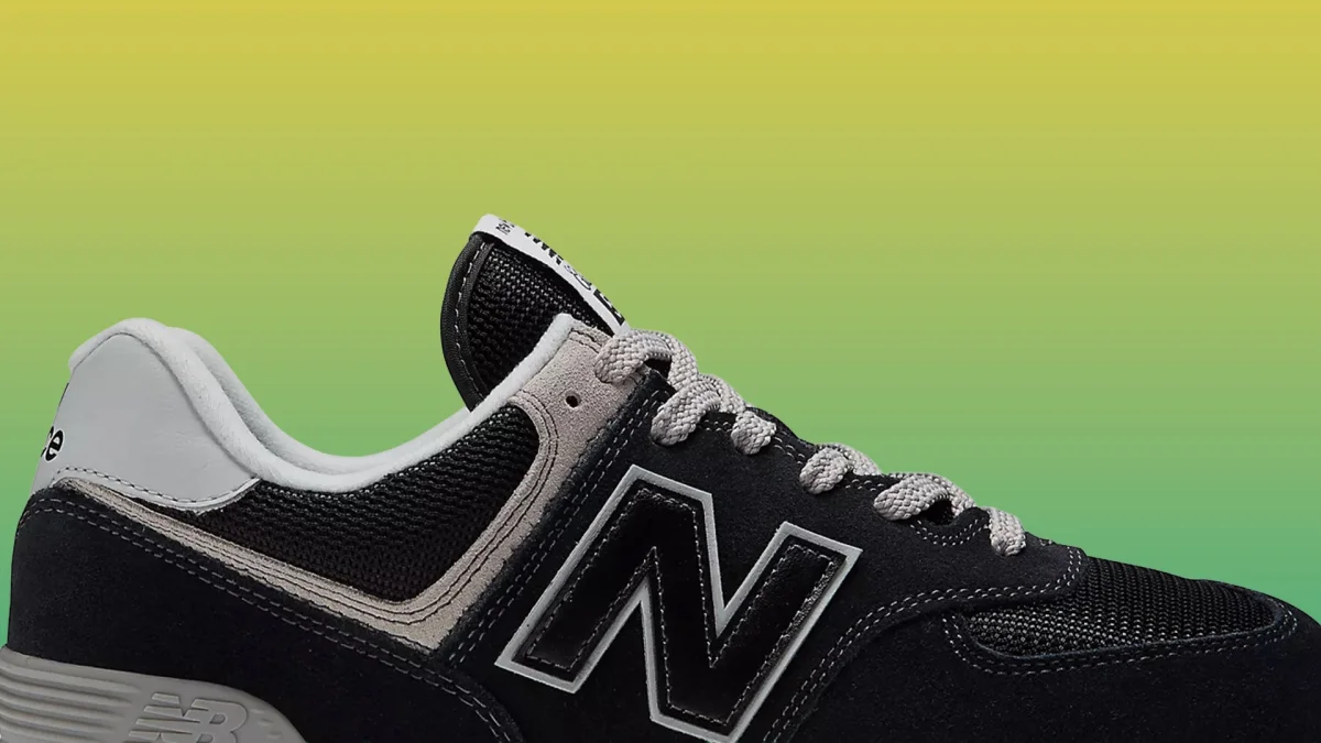 Close-up of black and gray New Balance sneaker with white laces and mesh fabric on a green-yellow gradient background.