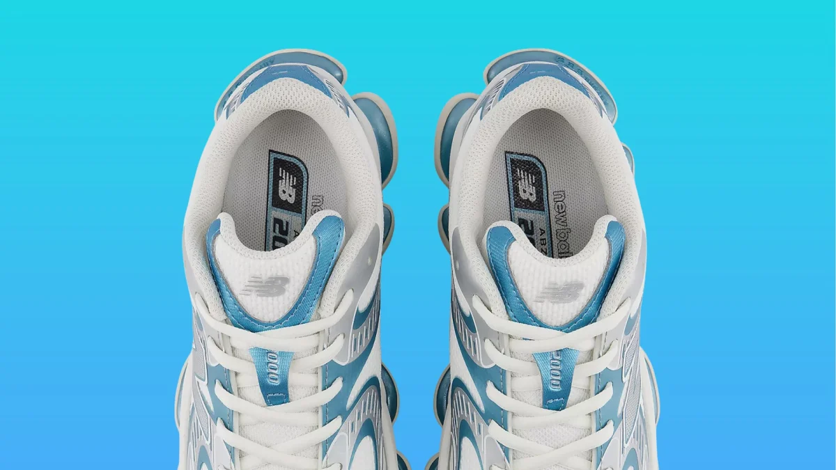 Top view of white and blue New Balance sneakers with visible insoles and laces against a blue background.