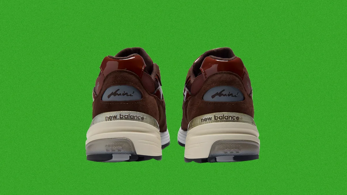 Brown New Balance sneakers viewed from the back, featuring cream-colored soles and set against a bright green background.
