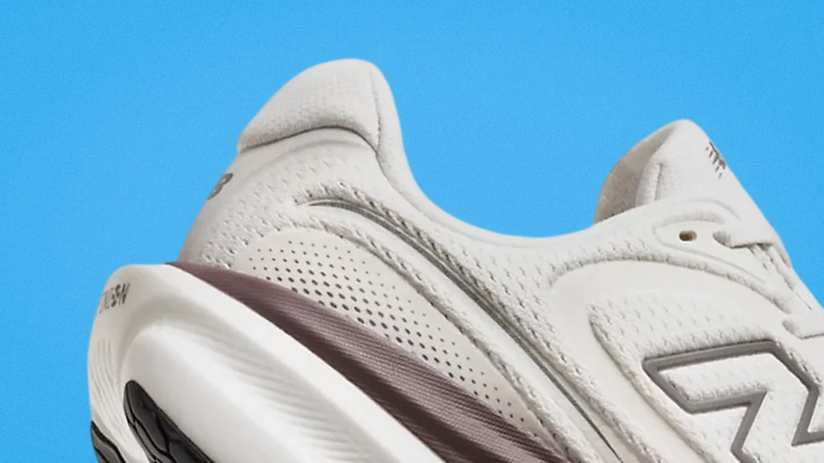 Close-up of the heel and side of a white New Balance sneaker with a maroon midsole against a blue background.