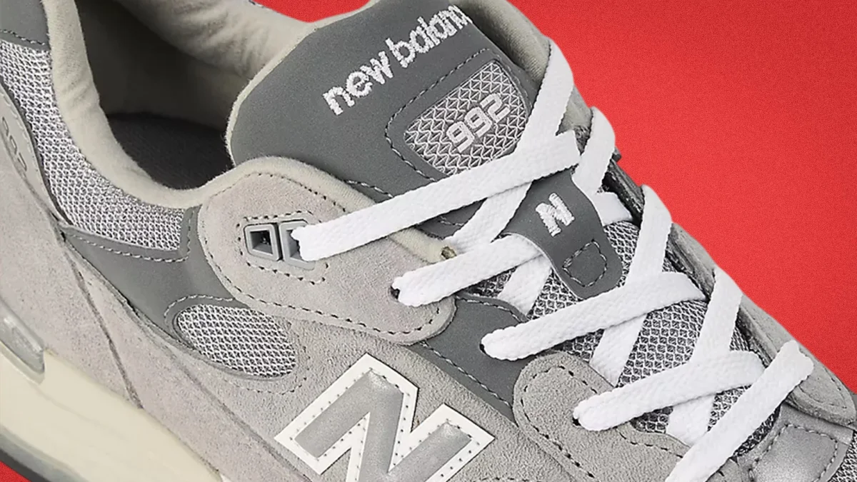 Gray New Balance 992 sneaker with white laces and mesh details on a red background.