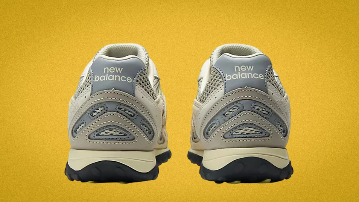 Pair of beige and gray New Balance sneakers shown from the back on a yellow background.