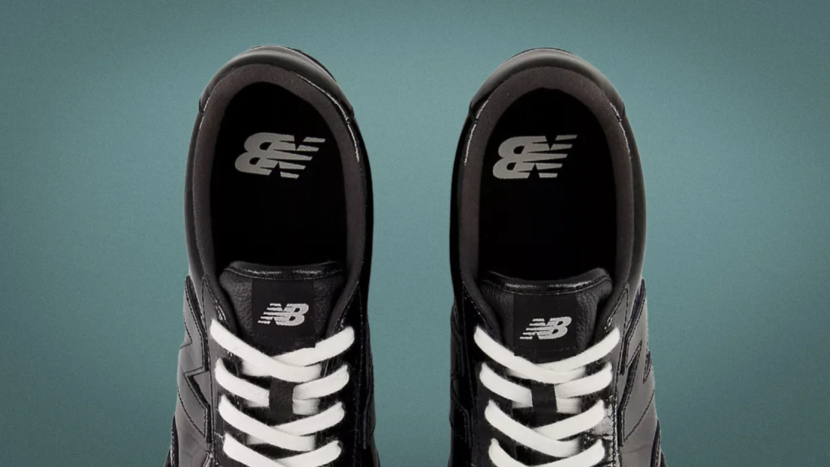 Pair of black New Balance sneakers with white laces viewed from above on a teal background.