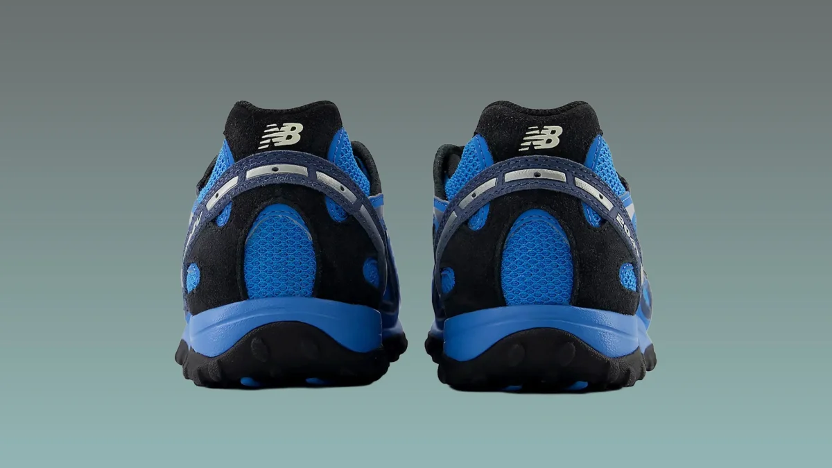 Pair of blue and black New Balance sneakers shown from the back on a gradient gray-green background.