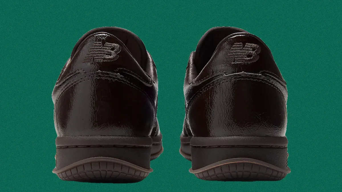 Pair of black shiny leather New Balance shoes shown from the back on a green background.