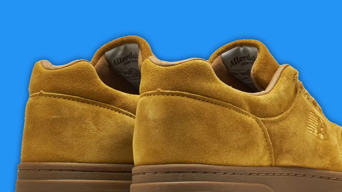 Pair of mustard yellow suede sneakers with brown rubber soles against a blue background.