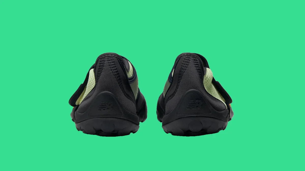 Pair of black and light green New Balance shoes viewed from the back on a green background.