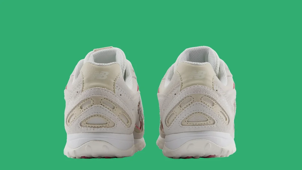 Pair of white New Balance sneakers viewed from the back on a solid green background.