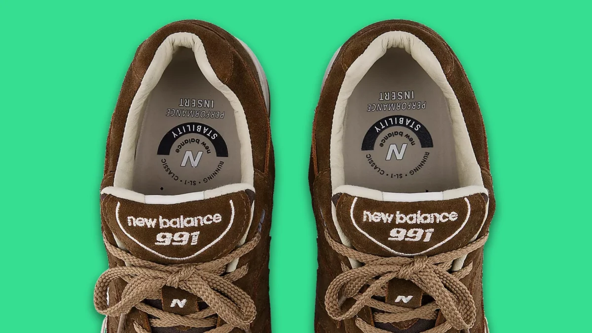 Pair of brown New Balance 991 sneakers seen from above on a bright green background, displaying visible branding and laces.