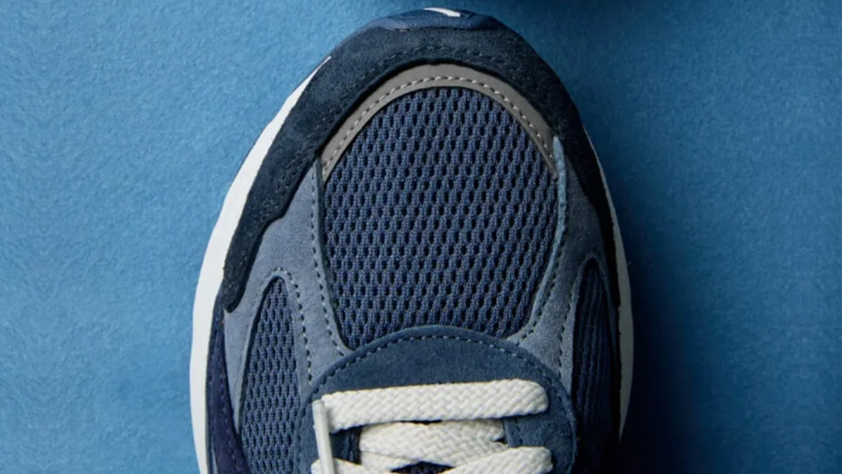 Close-up of a navy blue sneaker toe with mesh and suede panels and white laces on a blue surface.