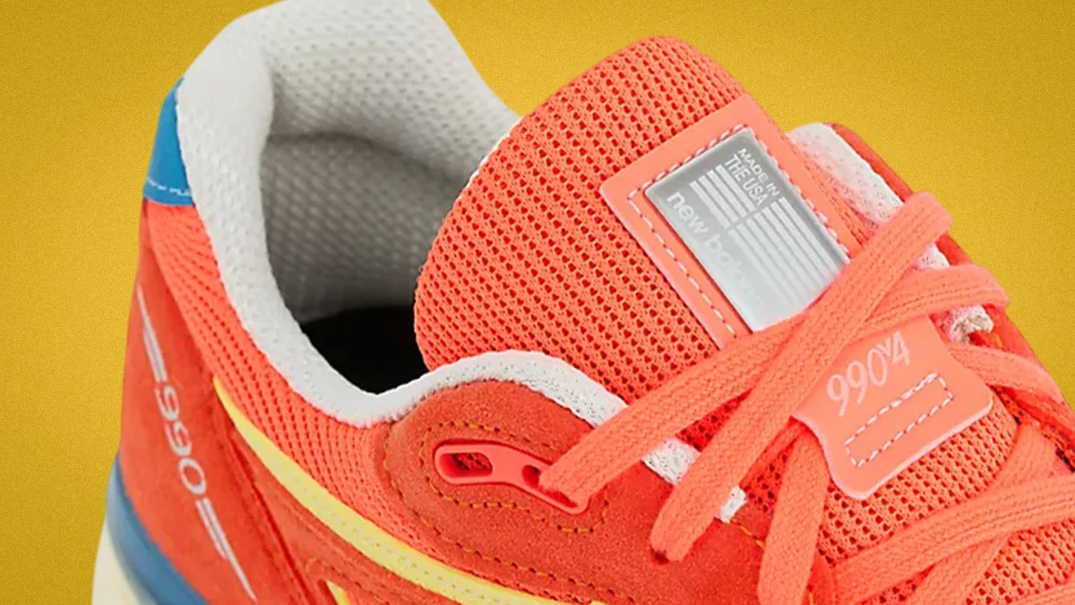 Close-up of an orange New Balance 990v4 sneaker with mesh tongue and white interior lining.