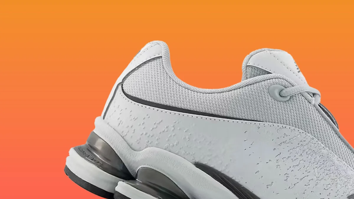 Close-up of a white and gray sneaker with mesh and textured leather upper against an orange background.