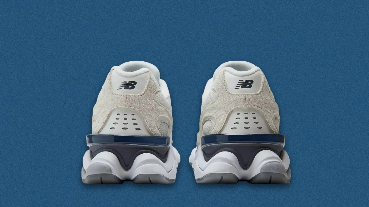 Pair of white and beige New Balance sneakers shown from the back on a blue background.