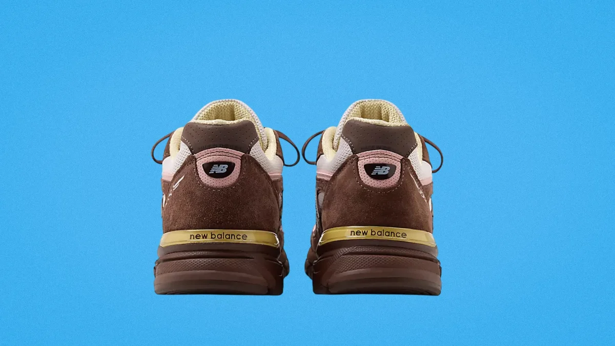 Pair of brown New Balance sneakers shown from the back with beige and pink accents on a blue background.