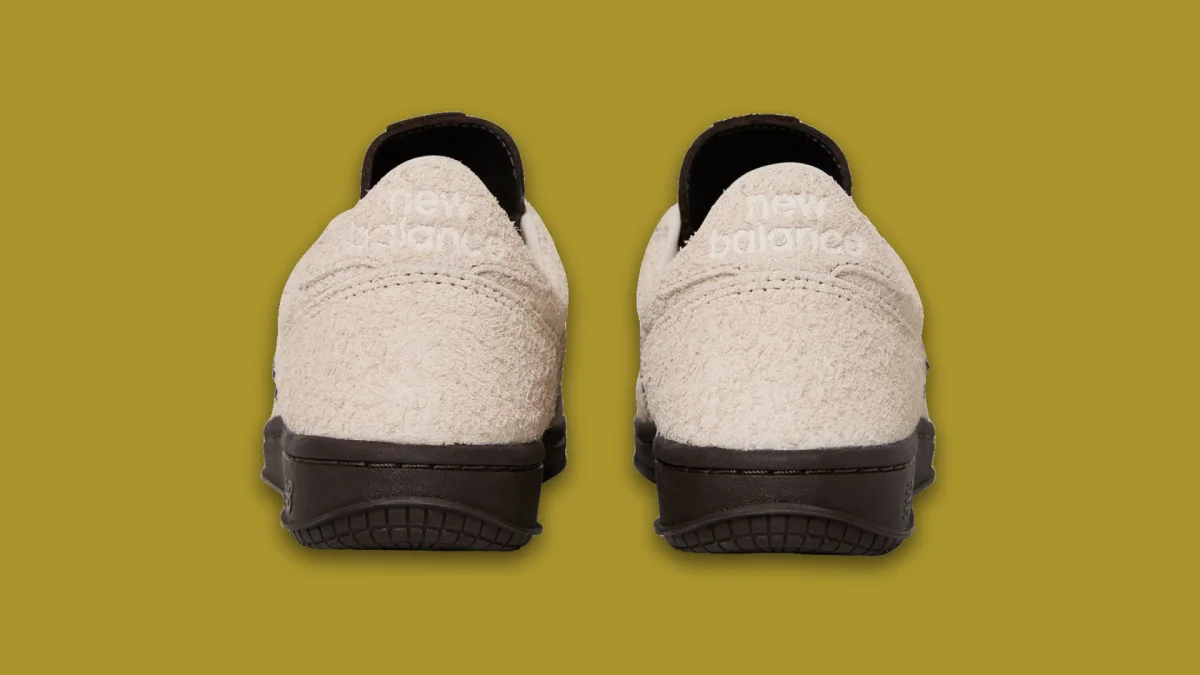 Back view of two beige suede New Balance sneakers with dark brown rubber soles.