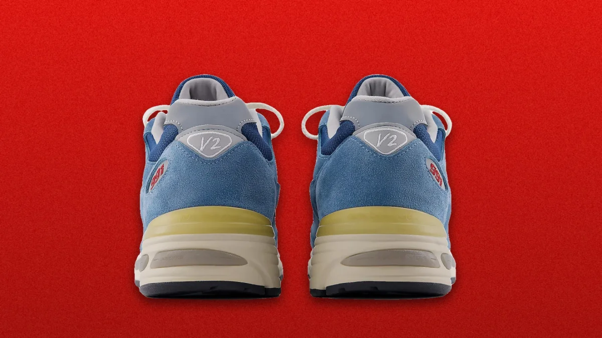 Blue and gray sneakers with white laces shown from the back on a solid red background, featuring V2 logos on the heels and light yellow midsoles.