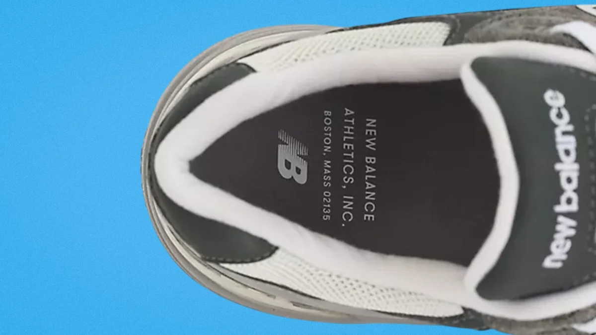 Top view of a New Balance sneaker with black insole and white padded collar on a blue background.