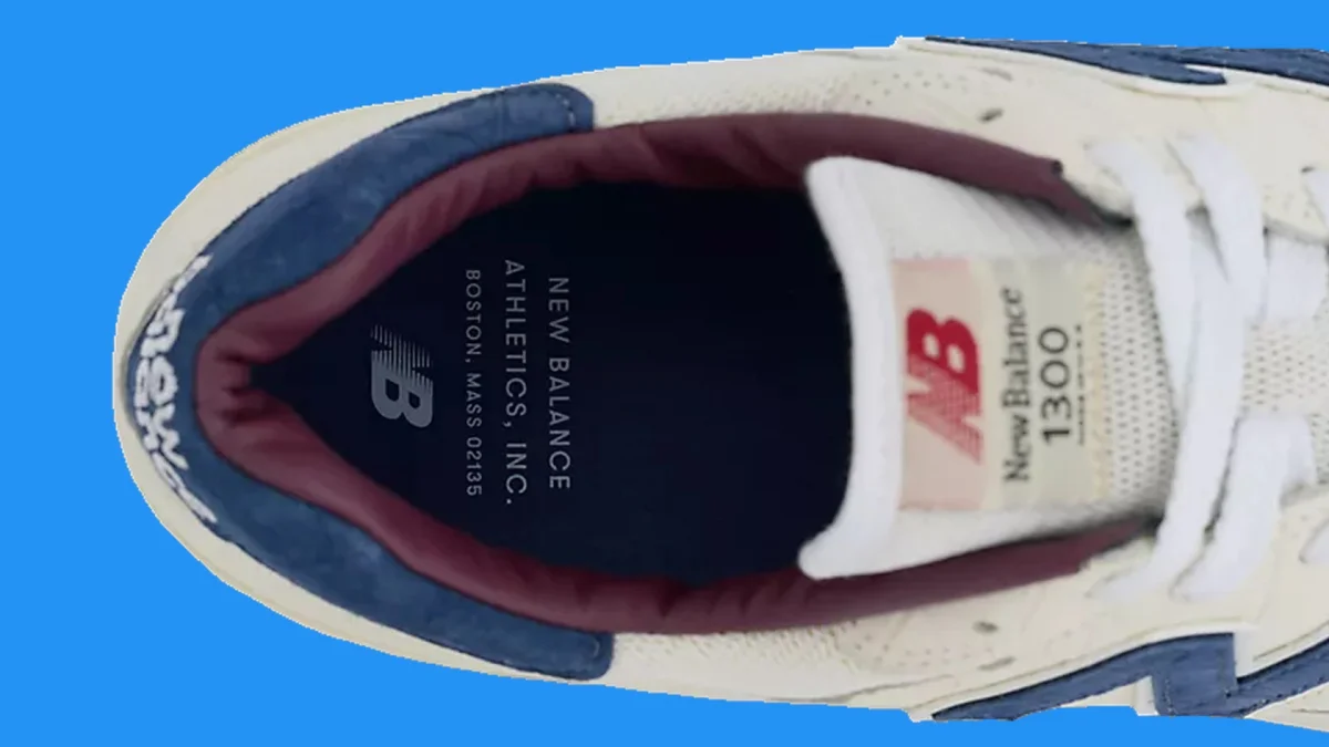 White and navy New Balance 1300 sneaker with maroon lining on a blue background.