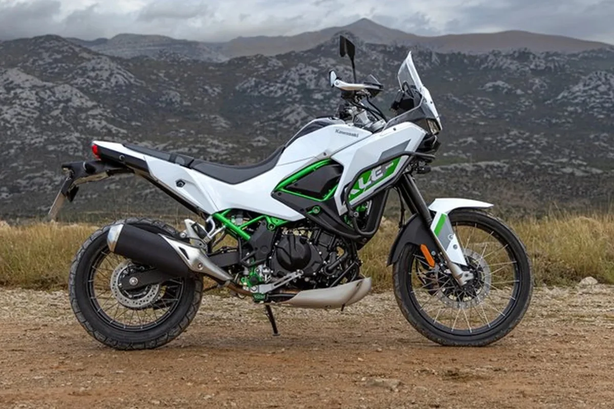 White and green Kawasaki Versys-X 300 motorcycle parked on a dirt path with mountains in the background.