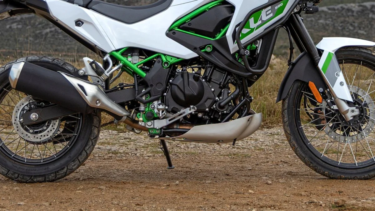 Side view of a white and green motorcycle with spoked wheels and a black exhaust, parked on a dirt path.