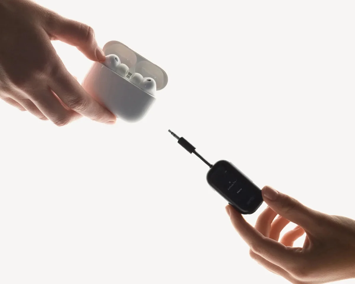 A white wireless earbud charging case and a black AirFly Bluetooth transmitter with an attached audio jack held in a hand.