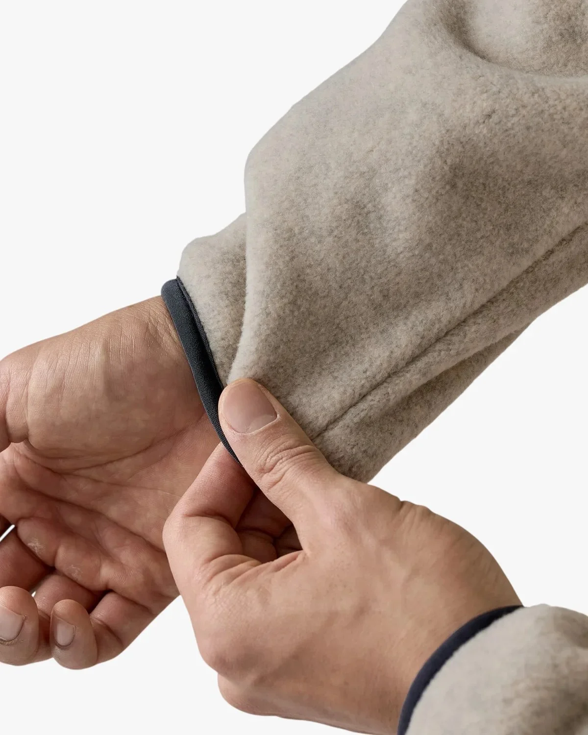 Close-up of a hand holding a beige fleece sleeve with a dark trim at the cuff.