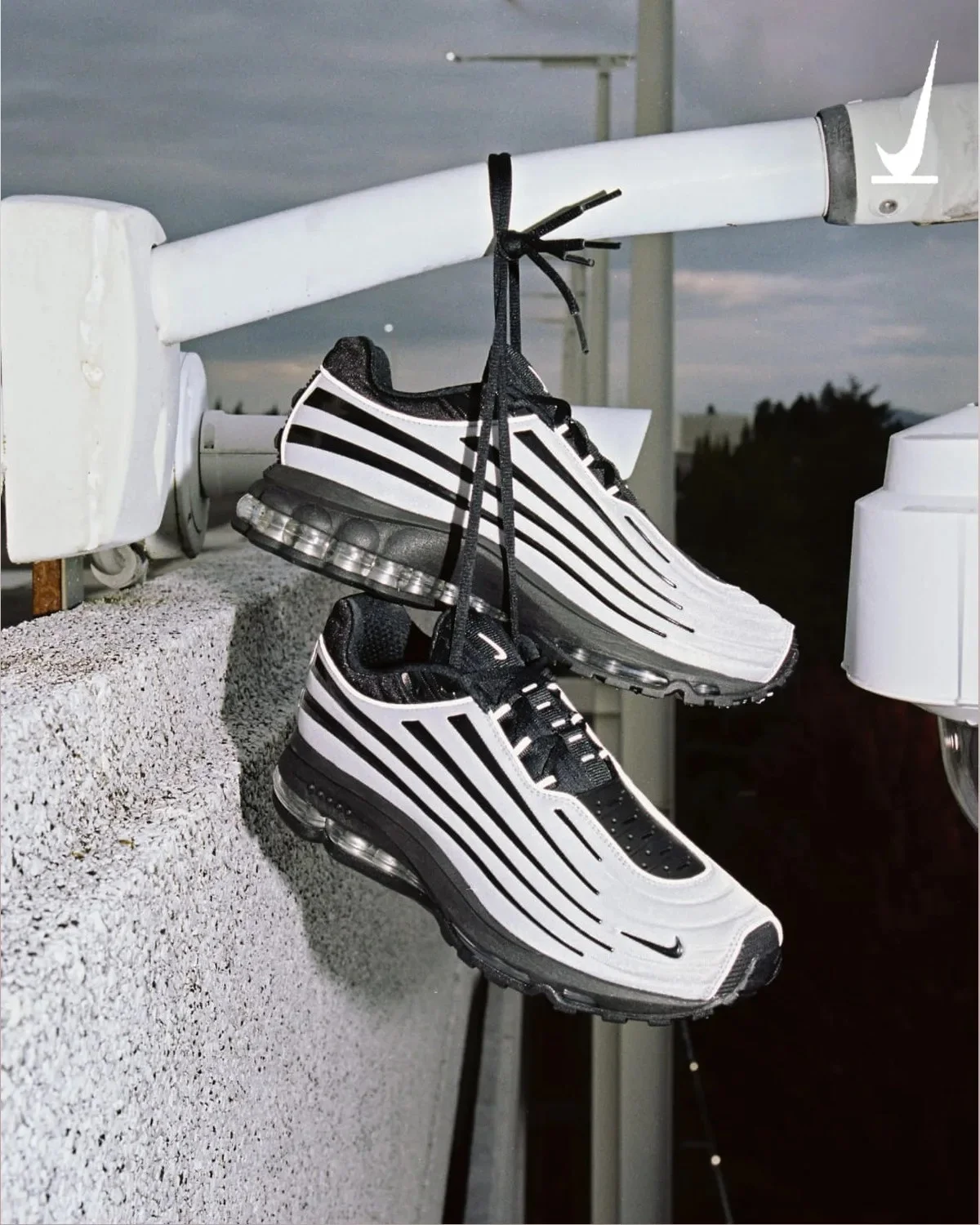 Black and white Nike Air Max sneakers with striped detailing, hanging by their laces from a white metal rail.