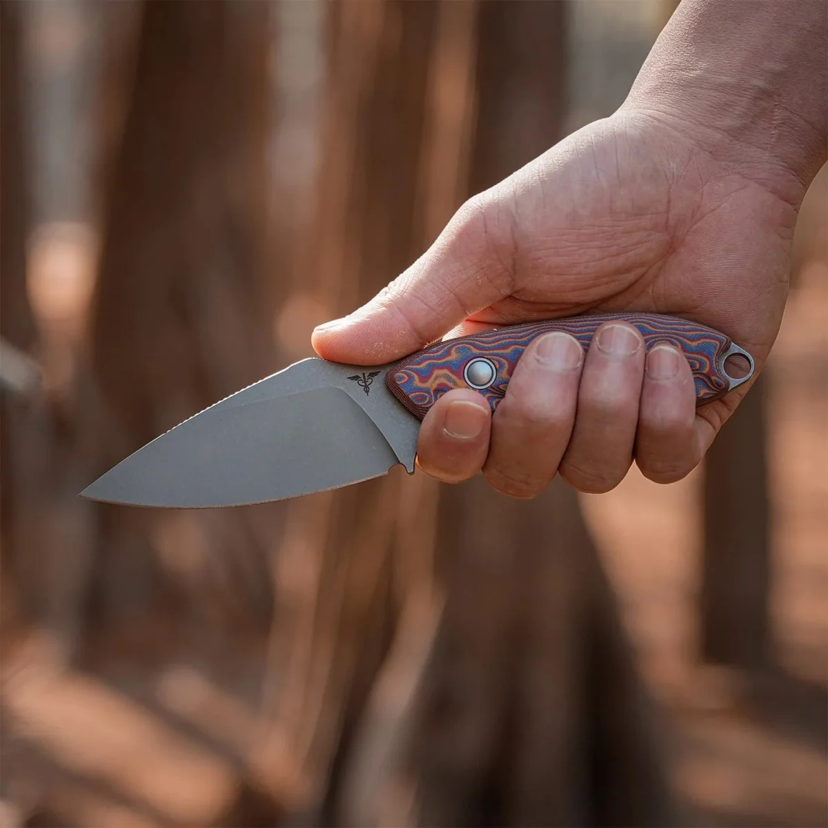 Hand holding a folding knife with a stonewashed blade and a colorful patterned handle.