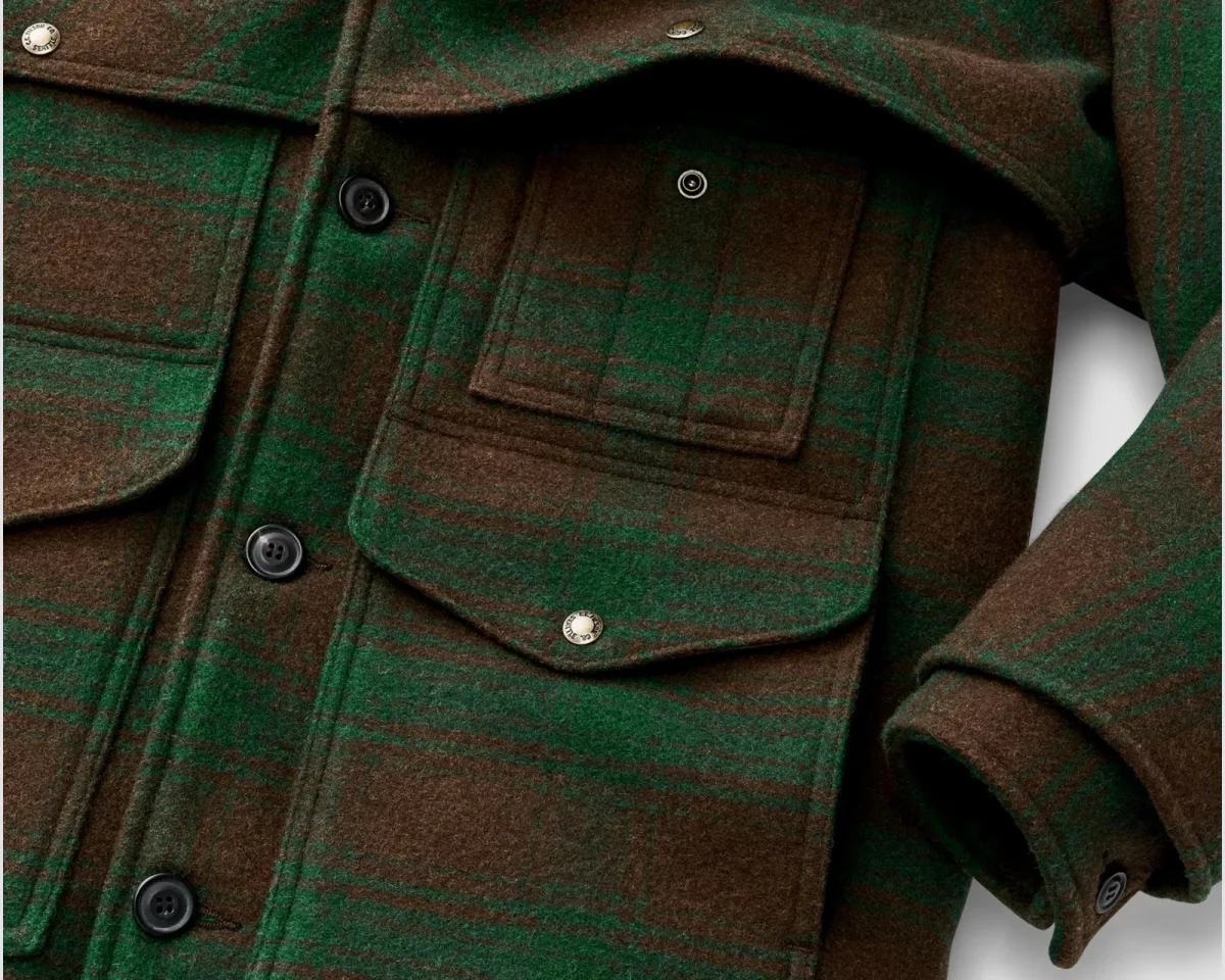 Close-up of a green and brown plaid wool-blend jacket featuring a front pocket with a metal snap button and dark buttons along the placket.