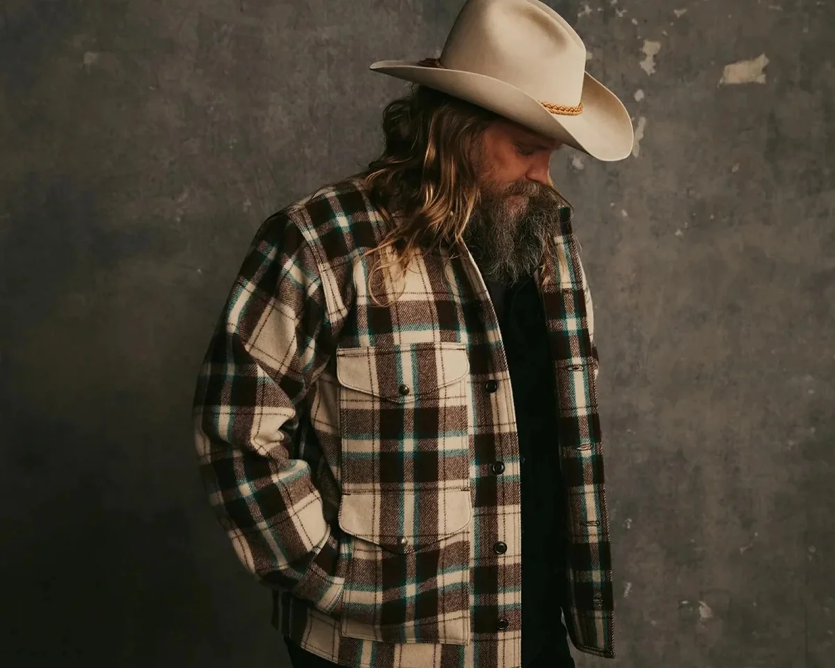 Beige cowboy hat and a brown, cream, and teal plaid button-down jacket with two chest pockets.