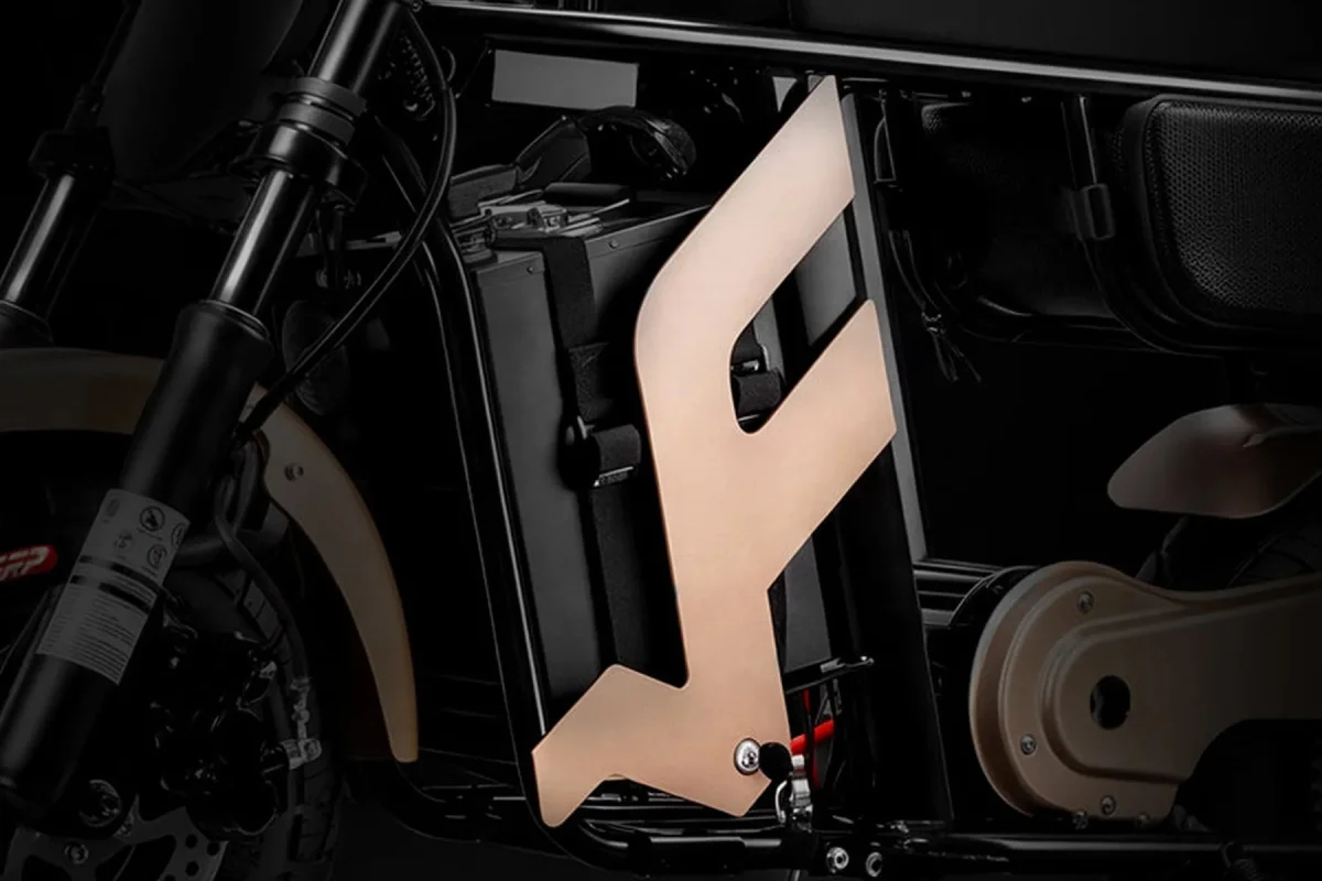 Close-up of an electric bike frame, featuring a prominent, angular, metallic copper-colored emblem mounted over a black battery pack.