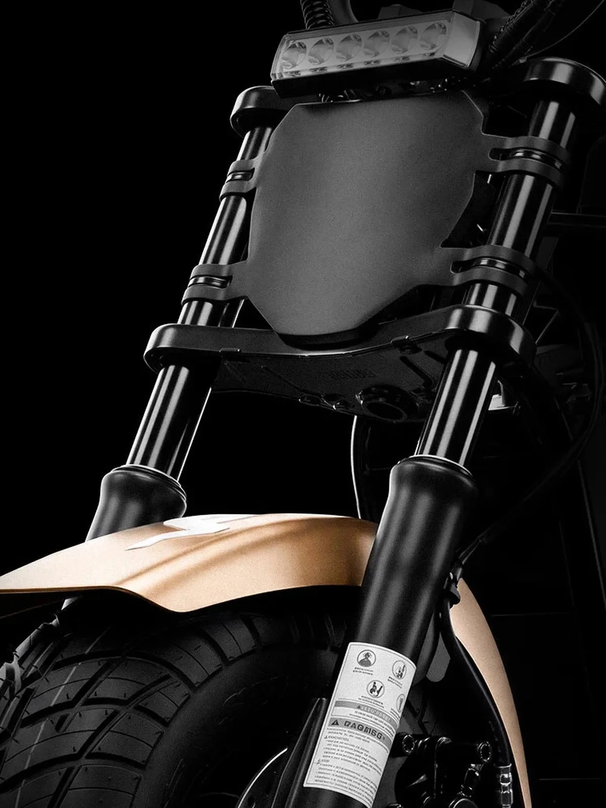 Front view of a motorcycle featuring black telescopic front forks, an LED headlight, and a gold-colored front fender positioned above a knobby tire.