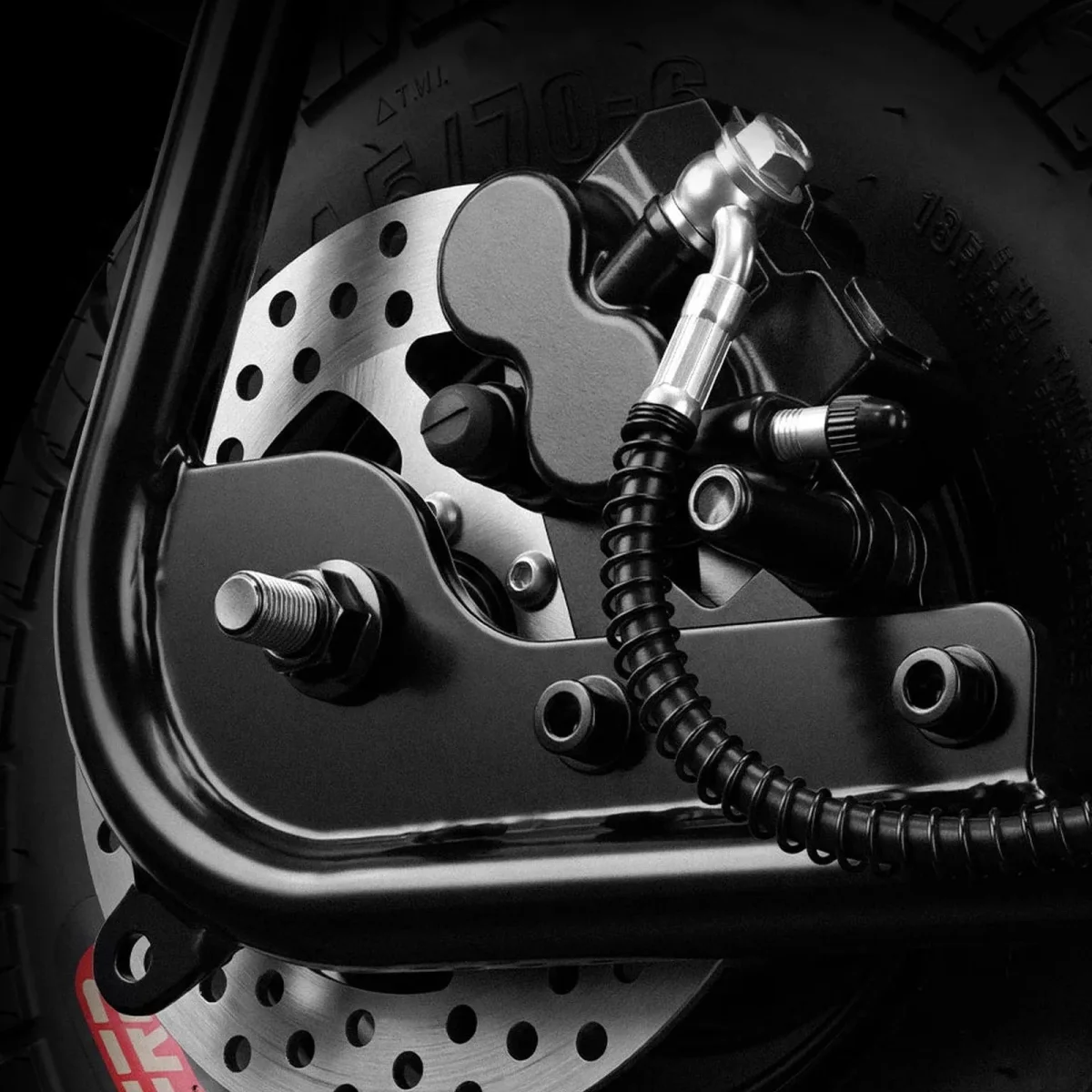 Close-up of a black motorcycle disc brake assembly featuring a silver perforated rotor and a black coiled hydraulic brake line.