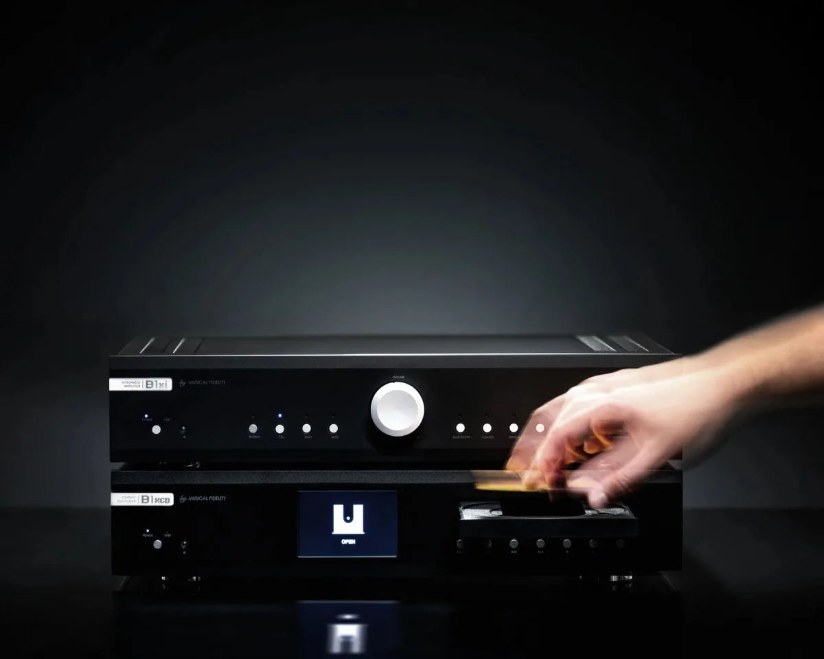 A disc is placed by a hand into the open tray of a Musical Fidelity B1xcd player, which is stacked beneath a matching Musical Fidelity B1si integrated amplifier.