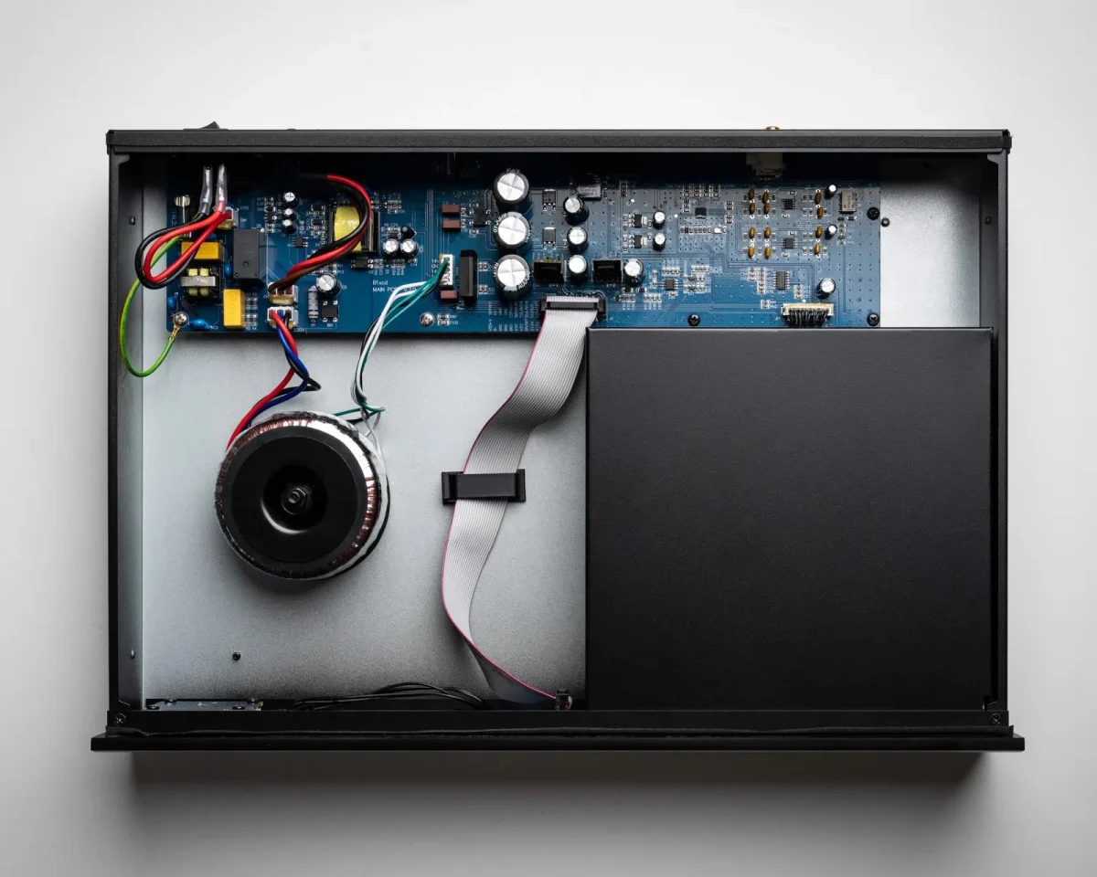 Internal view of an electronic device featuring a blue circuit board, a toroidal transformer, and a large black metal enclosure.