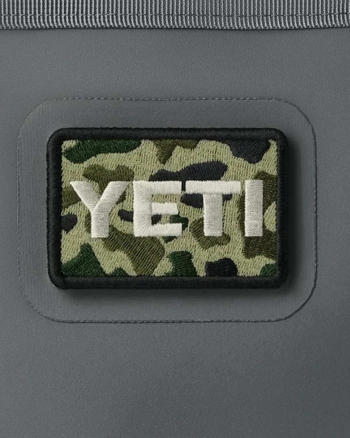 Rectangular Yeti patch featuring camo print embroidery, displayed on a grey surface.